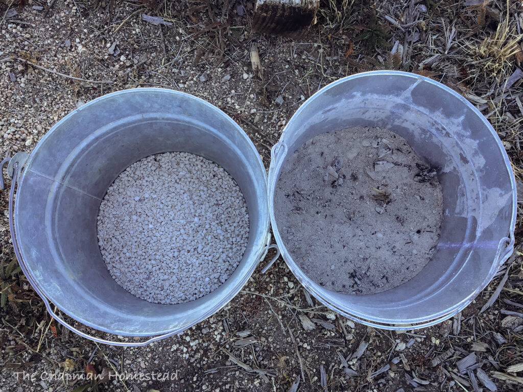 Picture of two metal buckets. The one on the left has oyster shell in it. The kind you would buy for chickens. The bucket on the right has wood ash in it.